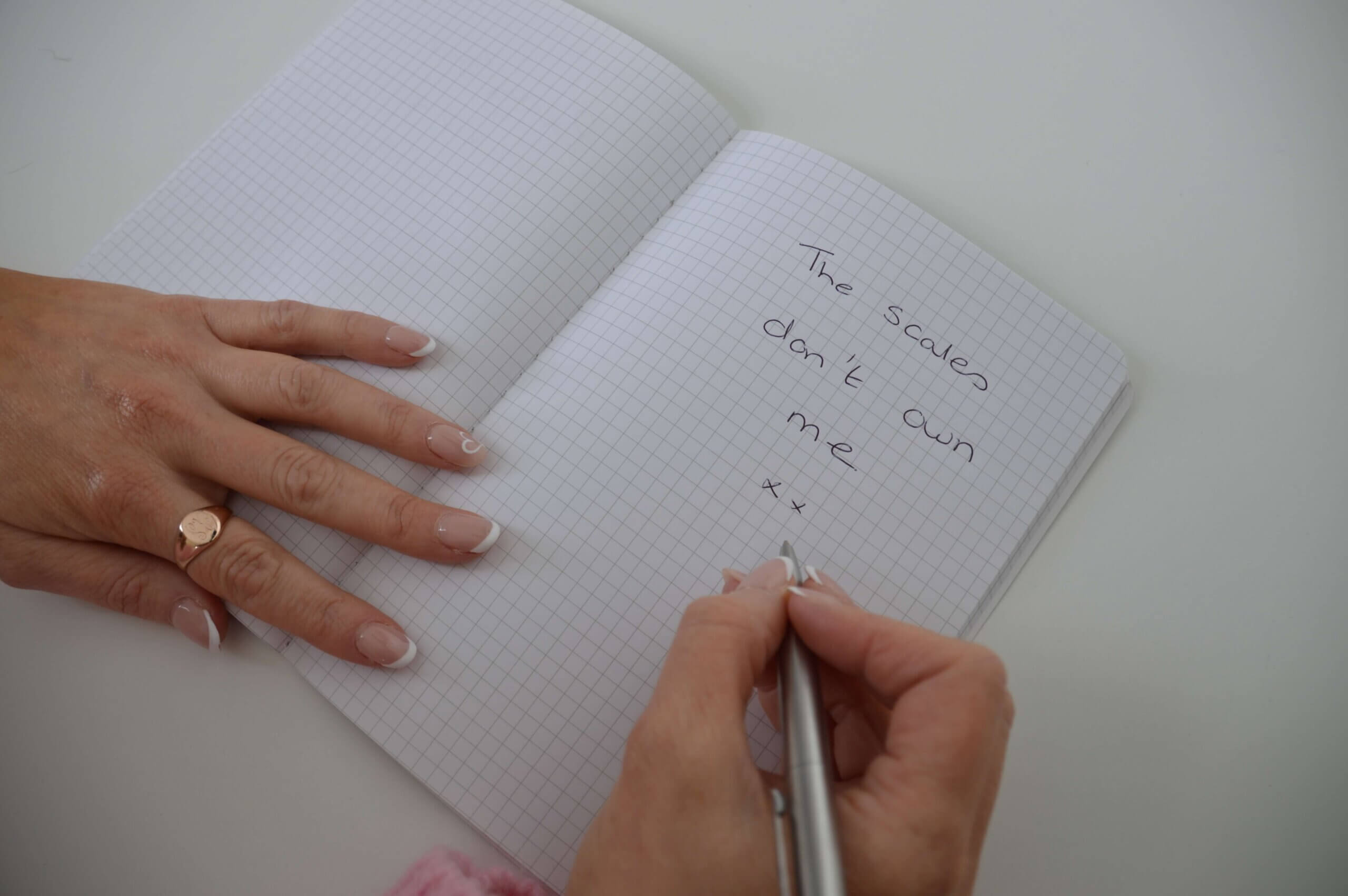 Person writing in a notebook that says "The scales don't own me" during eating disorder recovery