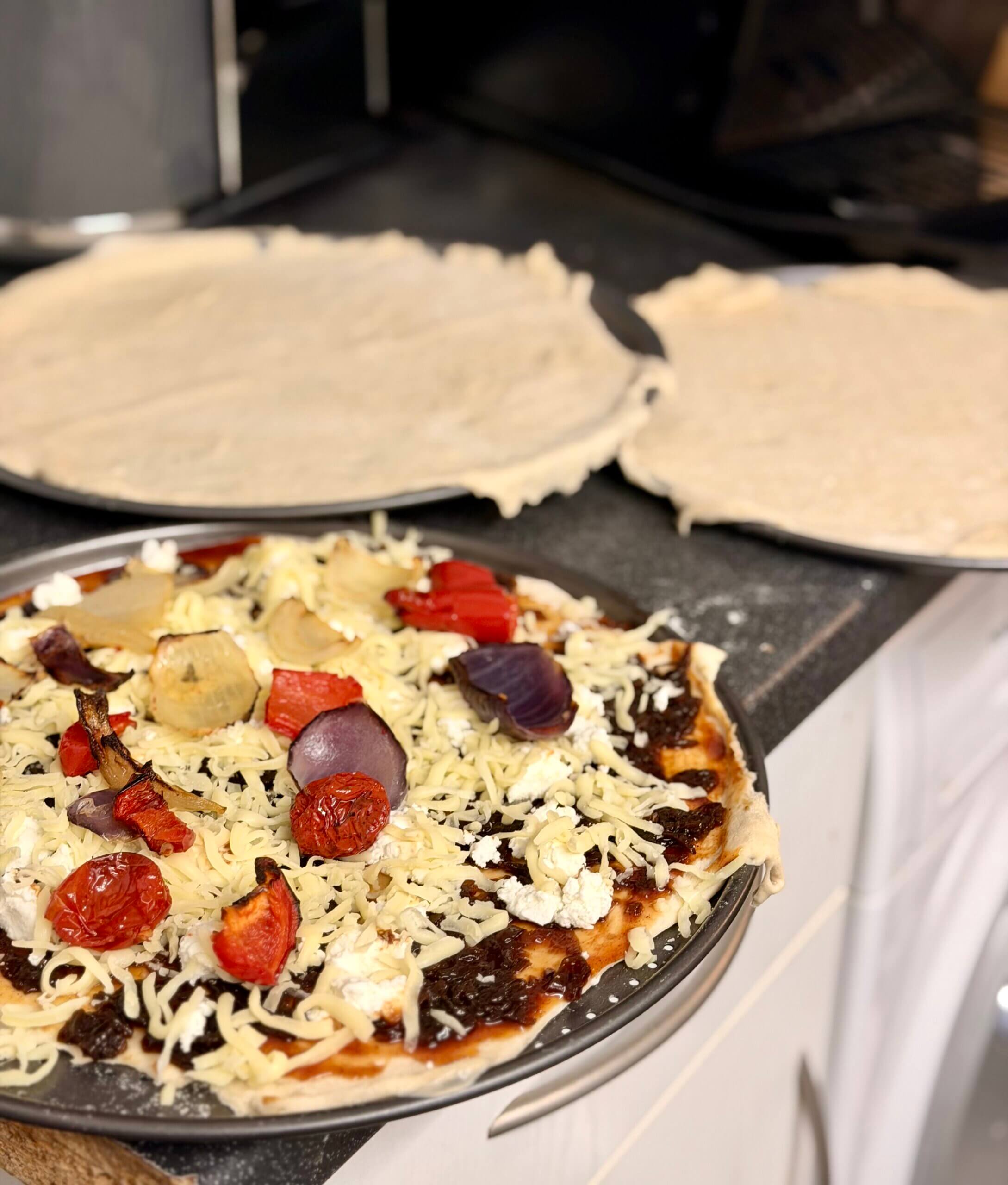 Homemade pizza being prepared with roasted red onions, tomatoes, peppers, and cheese on flatbread base